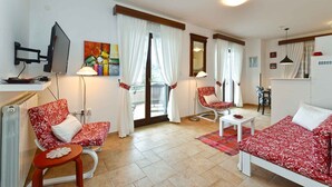 A well-lit living room with a sofa, chairs, a coffee table, and a TV. - Holiday apartment with pool, barbecue and fitness equipment for shared use (Barbariga)