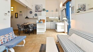 En kompakt opholdsstue med sofa, spisebord med stole, et tekøkken og et lille køkkenområde.