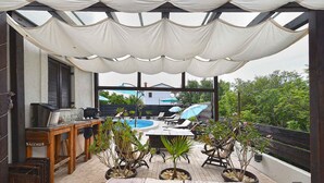 En overdækket terrasse med swimmingpool, liggestole og krukker med planter.