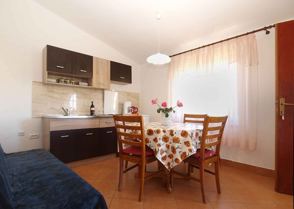 Una cocina compacta con armarios oscuros, una mesa de comedor con mantel floreado y una ventana con cortinas de encaje.