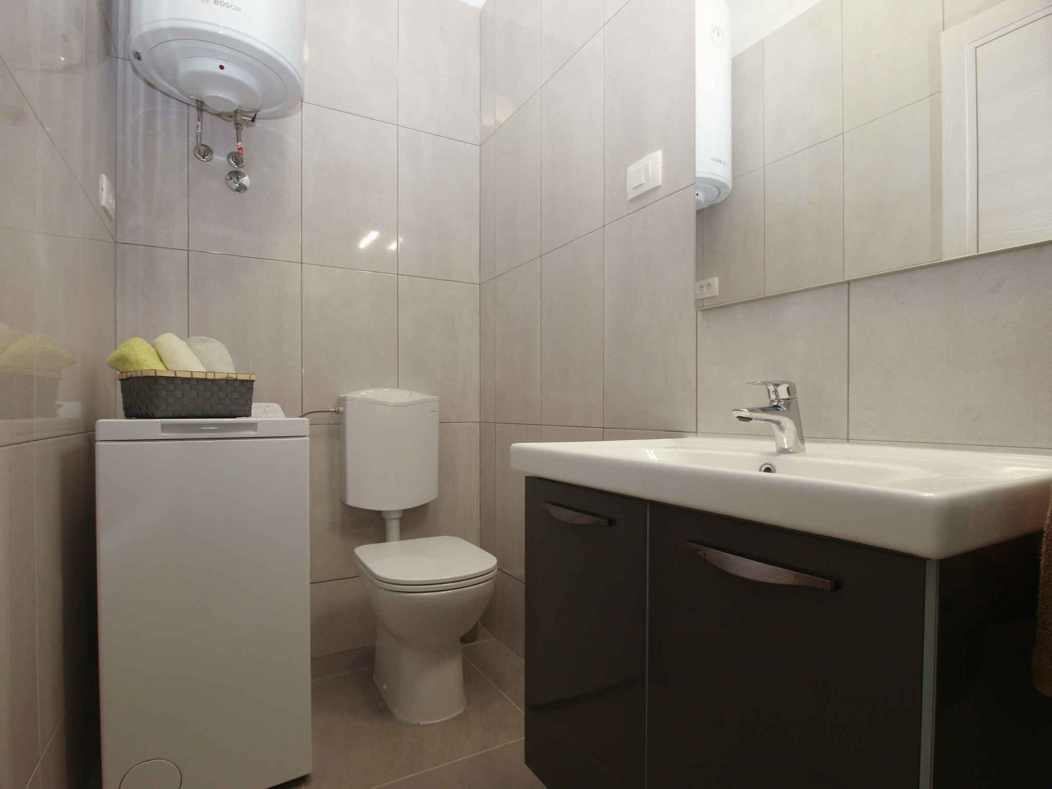 Een moderne badkamer met toilet, wastafel en een mandje verzorgingsproducten aan de linkerkant.