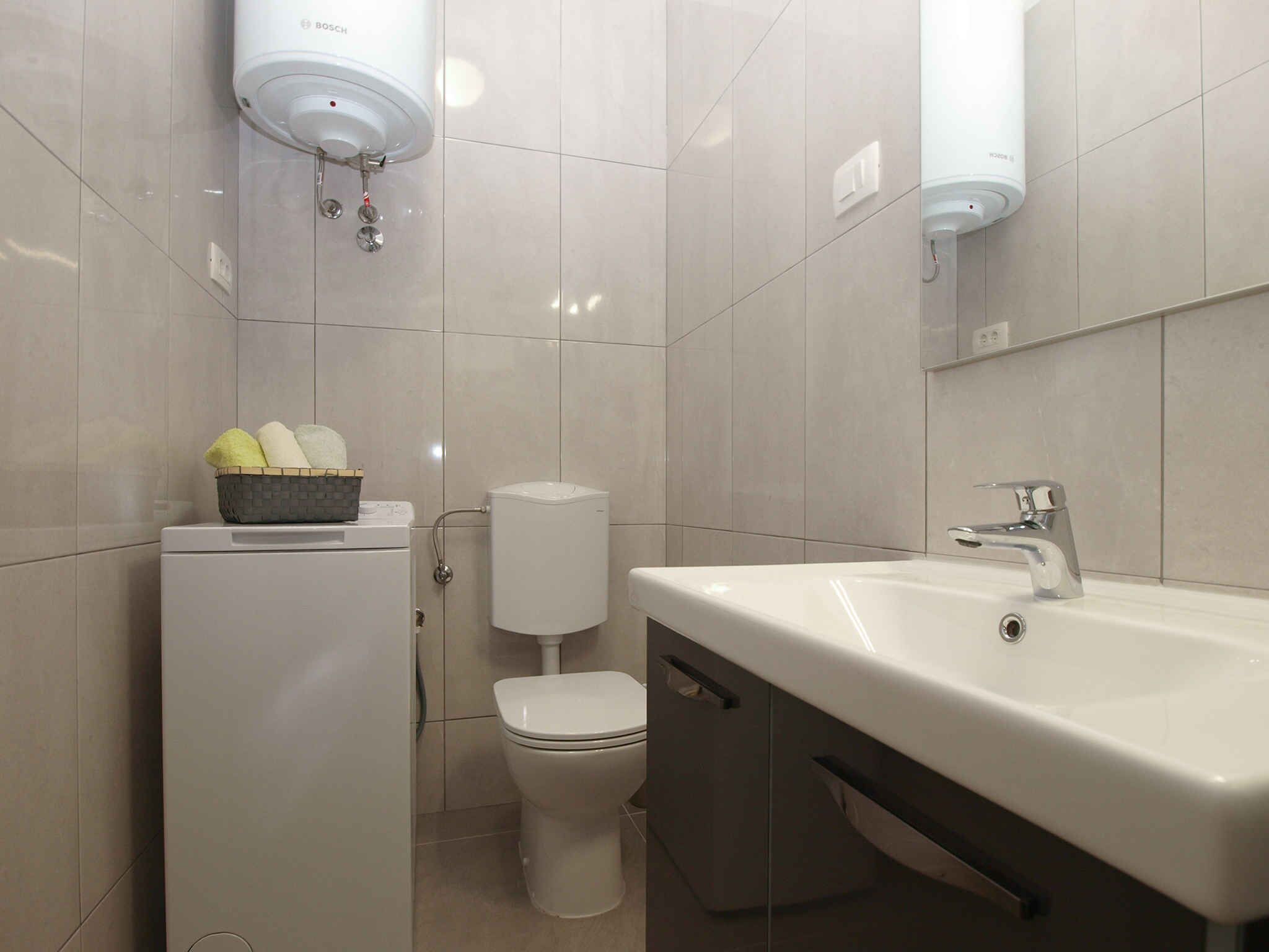 A modern bathroom with a white sink, toilet, and Bosch toilet paper dispenser.
