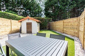 A patio area with a table and chairs, surrounded by wooden fences and a small shed. - Maison mitoyenne proche du lac ! (BISCARROSSE)
