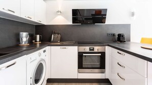 A modern kitchen with white cabinets, a built-in oven, a washing machine, and a coffee maker. - Maison mitoyenne proche du lac ! (BISCARROSSE)