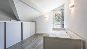 A small, modern room with a sloped ceiling, a window with curtains, and built-in cabinets. - Maison mitoyenne proche du lac ! (BISCARROSSE)