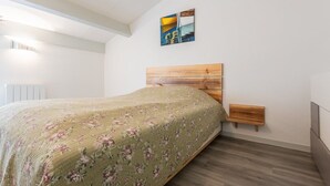 A bedroom with a wooden headboard, a green floral bedspread, and a small wooden bench beside the bed. - Maison mitoyenne proche du lac ! (BISCARROSSE)