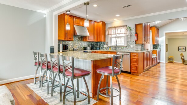 A spacious kitchen with wooden cabinets, a large island with bar stools, and a modern pendant light fixture.