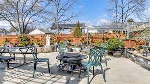 An outdoor patio area with a round table and chairs, surrounded by potted plants and a brick wall.