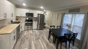 A modern kitchen with white cabinets, stainless steel appliances, and a dining area with a table and chairs. - Relax in our cozy, Pet-Friendly Country Escape/ Near Z-Plex & Downtown McKinney  (McKinney)