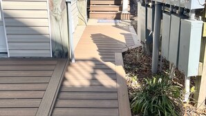 A wooden deck leading to a house with a visible staircase and electrical boxes.