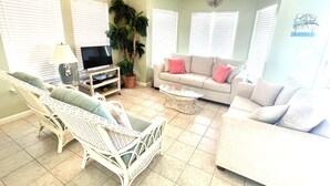 A living room with a white wicker chair, a beige sofa, and a television on a stand.