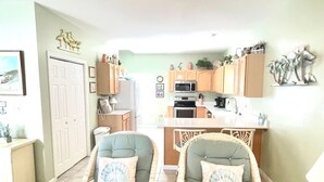 A spacious living area with two wicker chairs, a kitchen with wooden cabinets, and a ceiling fan.