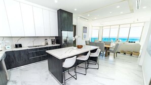 Una cocina moderna con encimera de mármol, una isla integrada con taburetes y vistas al mar a través de amplios ventanales.