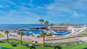 Un resort con varias piscinas, palmeras y vistas al océano.