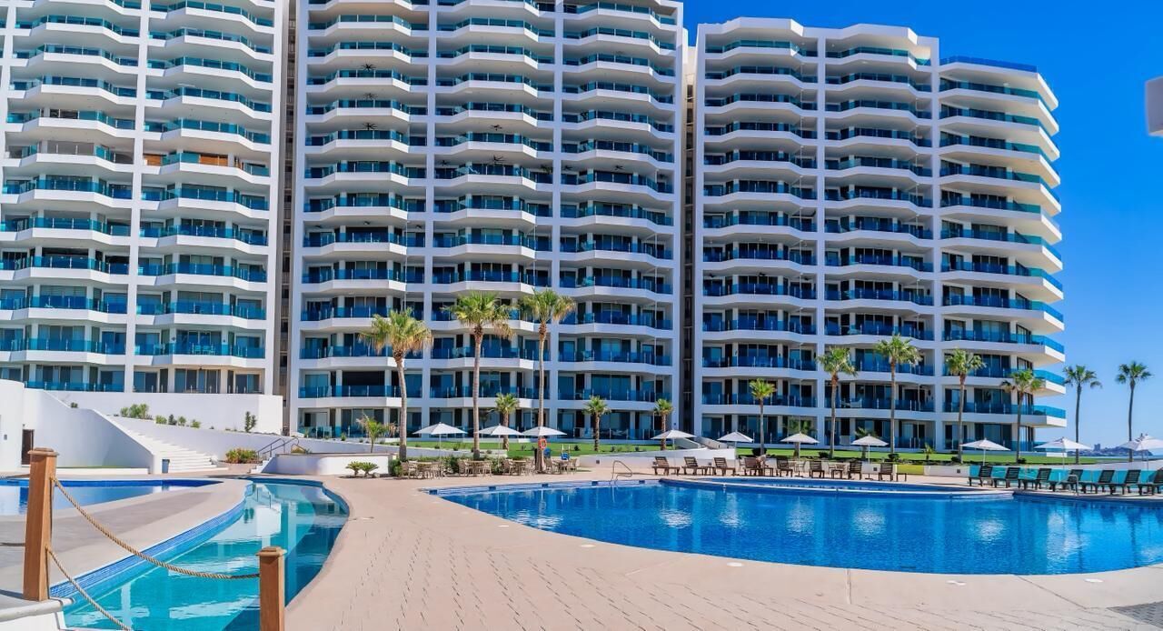 A multi-story hotel with a swimming pool, palm trees, and outdoor seating.
