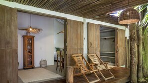 Quarto com piso de madeira, luminária pendente de vime, cadeiras de madeira e um armário com louças.