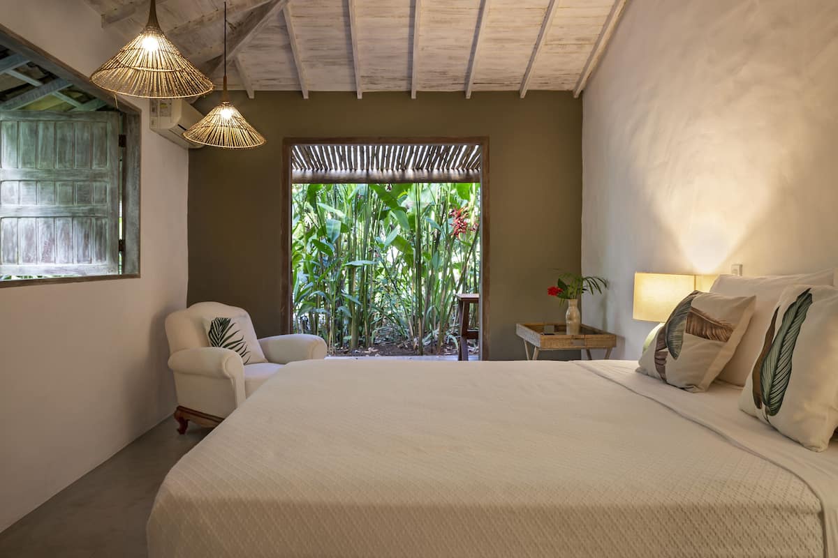 Une chambre avec un grand lit, une chaise, une table de chevet et une fenêtre donnant sur un paysage verdoyant.
