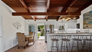 A kitchen with a wooden ceiling, white cabinets, and a large island with bar stools. - Sunset Vista | Private Dock, Dog-Friendly Home | My Beach Getaways (Pensacola Beach)
