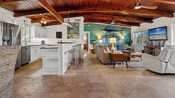 A spacious kitchen with white cabinets and stainless steel appliances, a dining area with a white sofa and wooden coffee table, and a living room with a TV and comfortable seating. - Sunset Vista | Private Dock, Dog-Friendly Home | My Beach Getaways (Pensacola Beach)