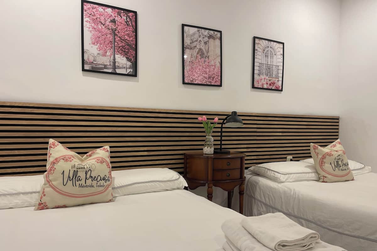 A hotel room with two beds, a wooden headboard, a nightstand with a lamp, and three framed pictures on the wall.