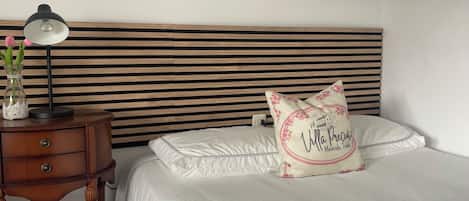 A neatly made bed with white linens, a bedside lamp, a vase with flowers, and a decorative pillow with text.