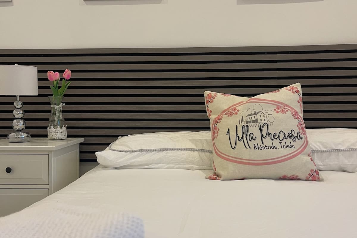 A neatly made bed with a decorative pillow, a bedside table with a lamp and vase, and framed artwork on the wall.