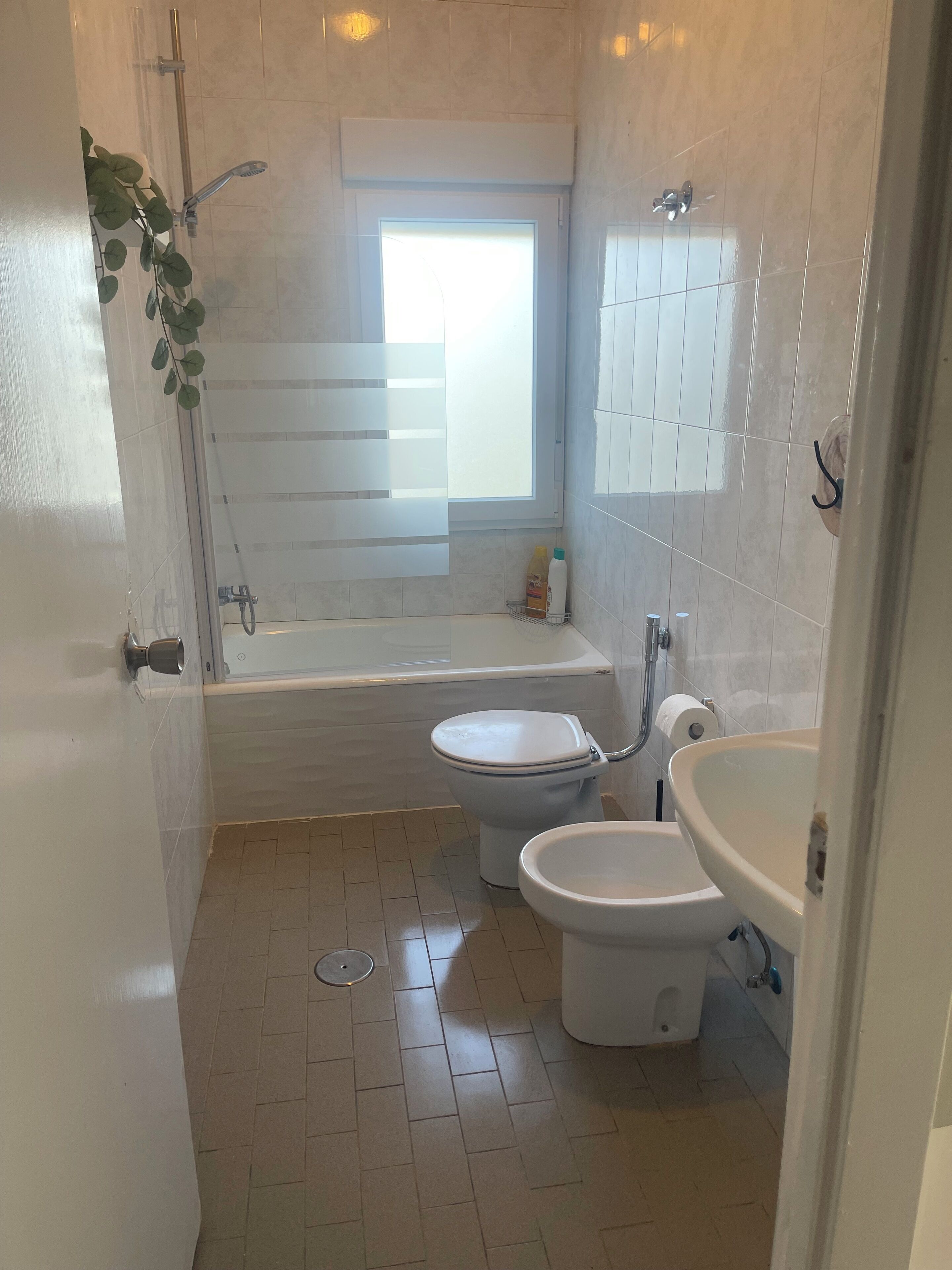 A bathroom with a bathtub, two toilets, a sink, and a window.