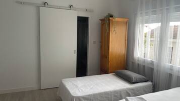Un dormitorio con dos camas, un armario y una ventana con cortinas translúcidas.