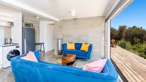 A modern kitchen with a washing machine, a refrigerator, and a dining area with a blue sofa and orange cushions. - Secluded Haven with Stunning Hokianga Harbour Views (Omapere)