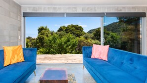A modern outdoor seating area with two blue sofas, each with a pillow, a wooden coffee table, and a patterned rug. - Secluded Haven with Stunning Hokianga Harbour Views (Omapere)