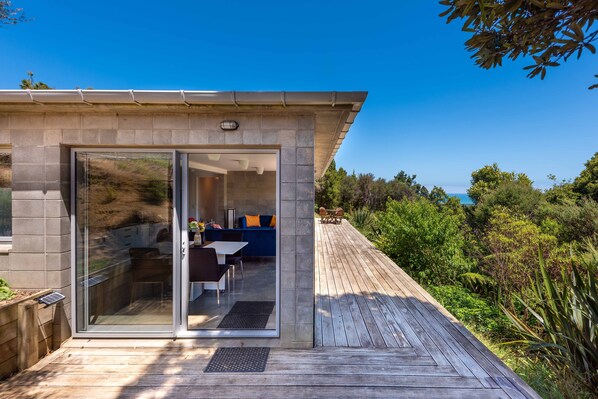 Una casa moderna con un ventanal de vidrio que da a un patio con mobiliario exterior.