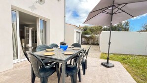 Eine Terrasse mit Tisch für vier Personen, Gartenstühlen, einem Grill und einem großen Sonnenschirm.