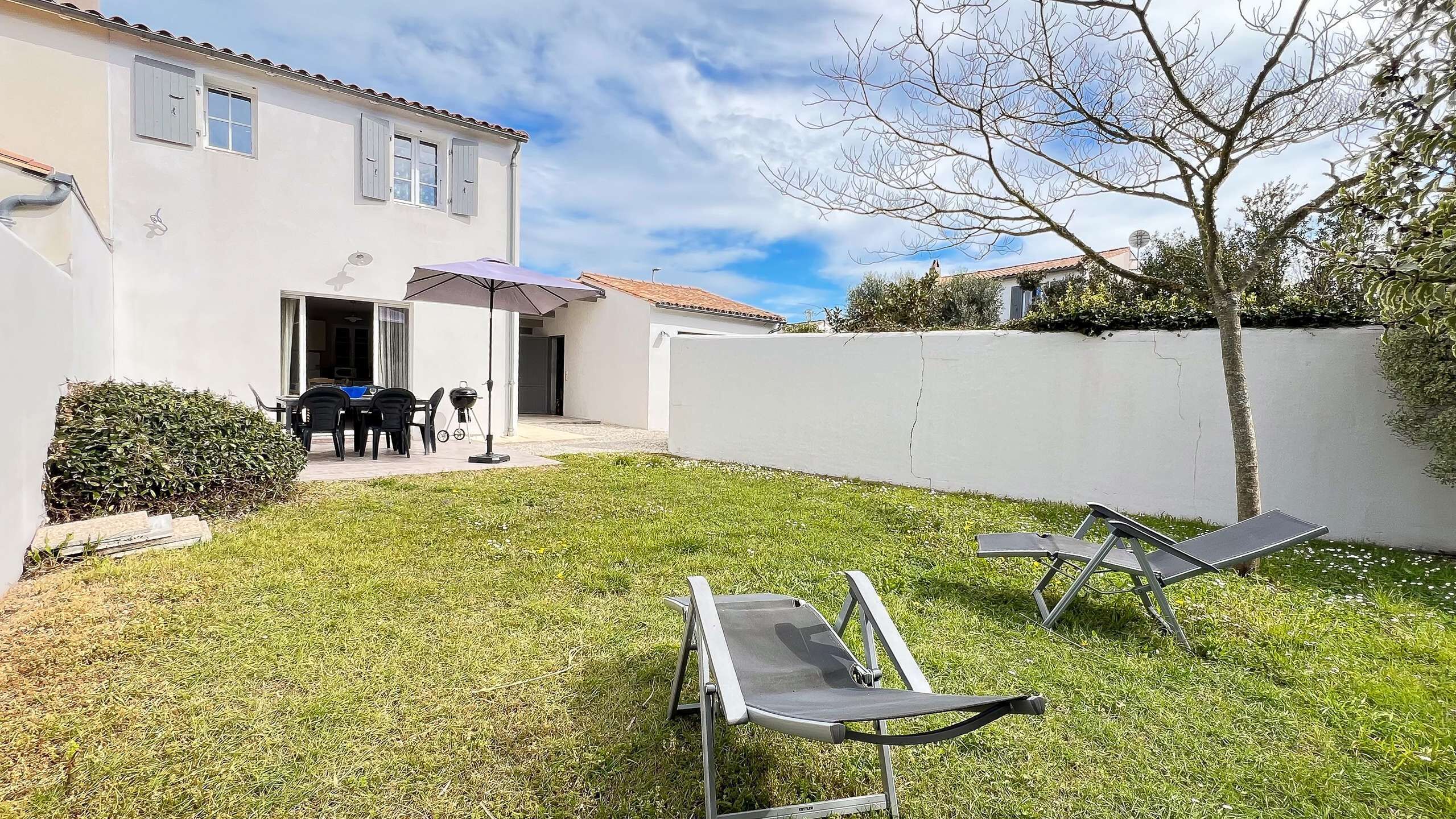 A backyard with a patio, a grill, and a white wall.