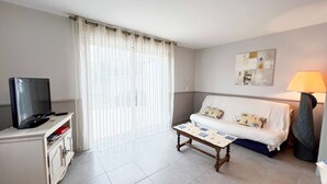 Ein Hotelzimmer mit Fernseher auf einem Schrank, einer Couch mit Kissen, einem kleinen Tisch und einer Lampe.