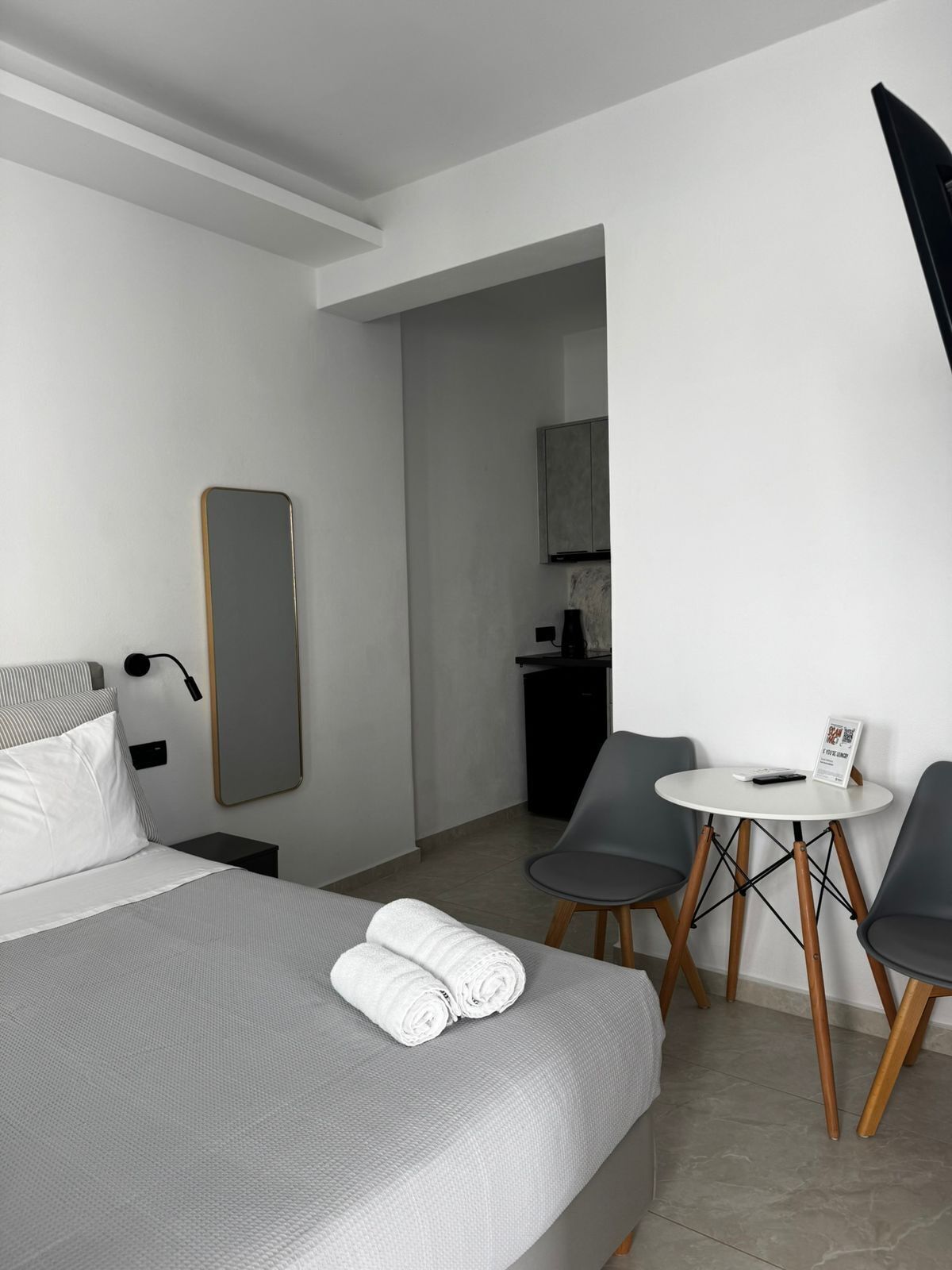 Een moderne hotelkamer met een bed, een klein tafeltje met stoelen, een bureau en een spiegel.