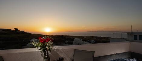 A balcony with a table set for two, a vase with flowers, a bottle of wine, and a glass of wine.