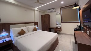 A modern hotel room with a neatly made bed, a wooden nightstand, a desk with a chair, a large mirror, and a ceiling fan. - Nexstay Kites Inn (Bengaluru)