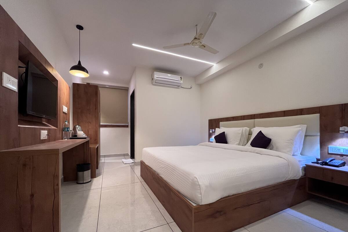 Quarto de hotel moderno com estrutura de cama em madeira, televisão de tela plana na parede, ventilador de teto e mesa de cabeceira com luminária.