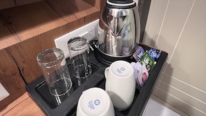 A kitchen area with a coffee maker, a kettle, a glass, and a tray with snacks. - Nexstay Kites Inn (Bengaluru)