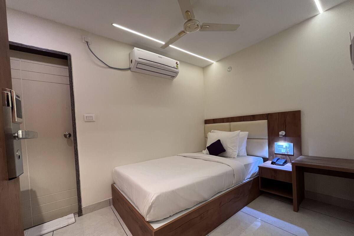 Quarto de hotel com cama, mesa de cabeceira, ventoinha de teto, ar condicionado e uma porta.