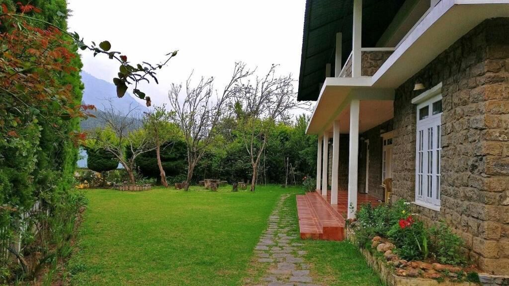 A stone house with a green roof, a paved pathway, and a well-maintained garden.