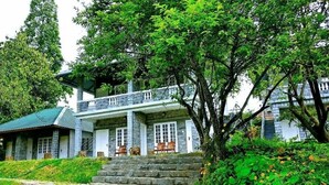 A two-story stone building with a balcony, surrounded by lush greenery. - Nexstay Ministers Mansion (Devikolam)