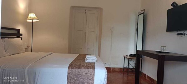 A hotel room with a bed, a desk, a chair, a lamp, a TV, and a door. - Nexstay Ministers Mansion (Devikolam)