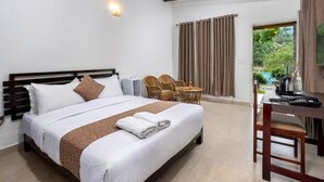 A hotel room with a bed, a desk, and chairs. There is a window with curtains and a view of greenery outside. - Nexstay Ministers Mansion (Devikolam)