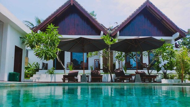 A poolside area with two wooden structures, a pool, and outdoor seating. - THELOCAL AREGULING  (Kuta)