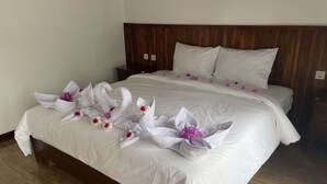 A neatly made bed with white linens and decorative towels shaped like swans with purple flowers. - THELOCAL AREGULING  (Kuta)