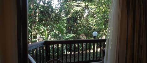 A balcony with a wooden railing, a chair, and a view of lush greenery outside.