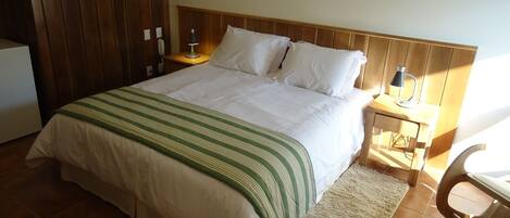 A neatly made bed with a striped bedspread, a wooden headboard, a bedside table with a lamp, and a chair.