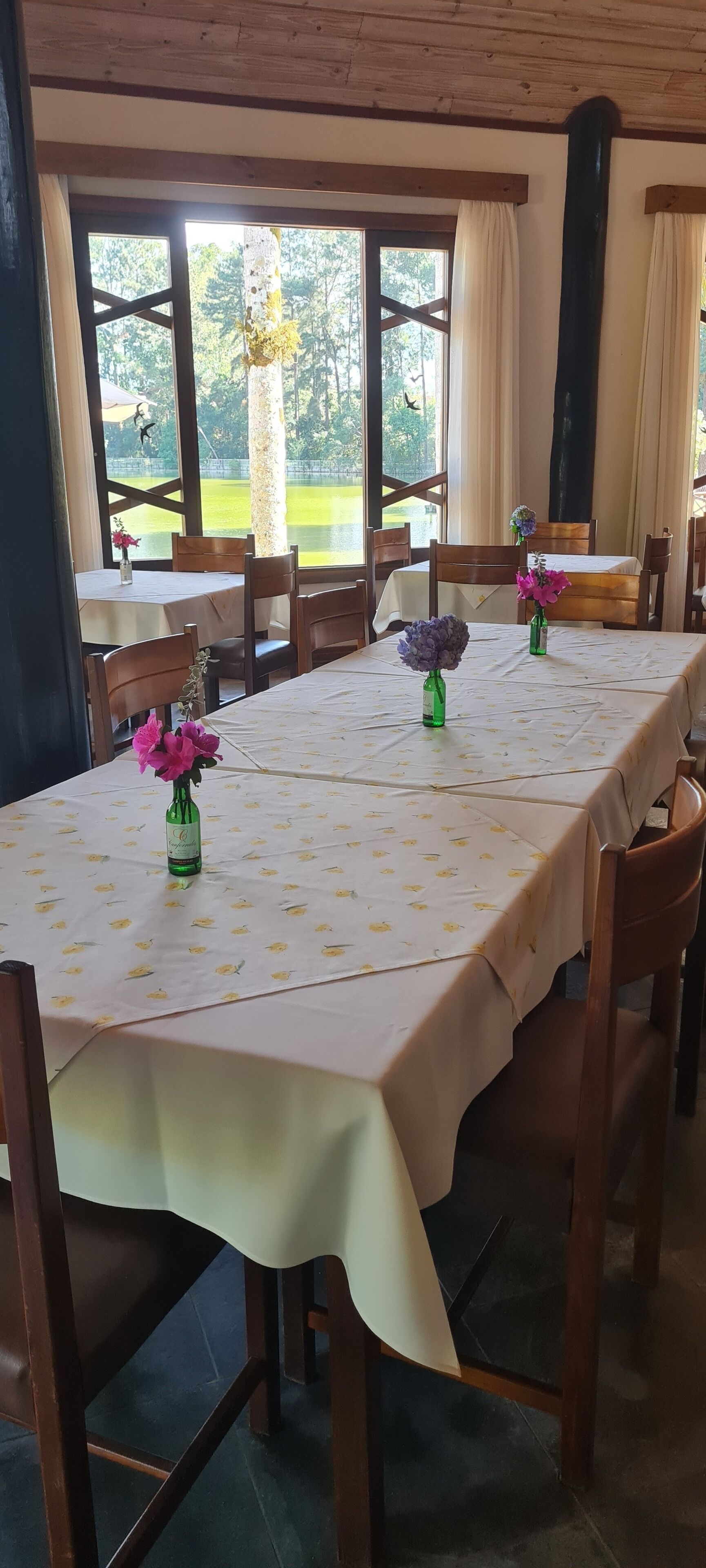 A dining area with a long table covered in a floral tablecloth, surrounded by wooden chairs.