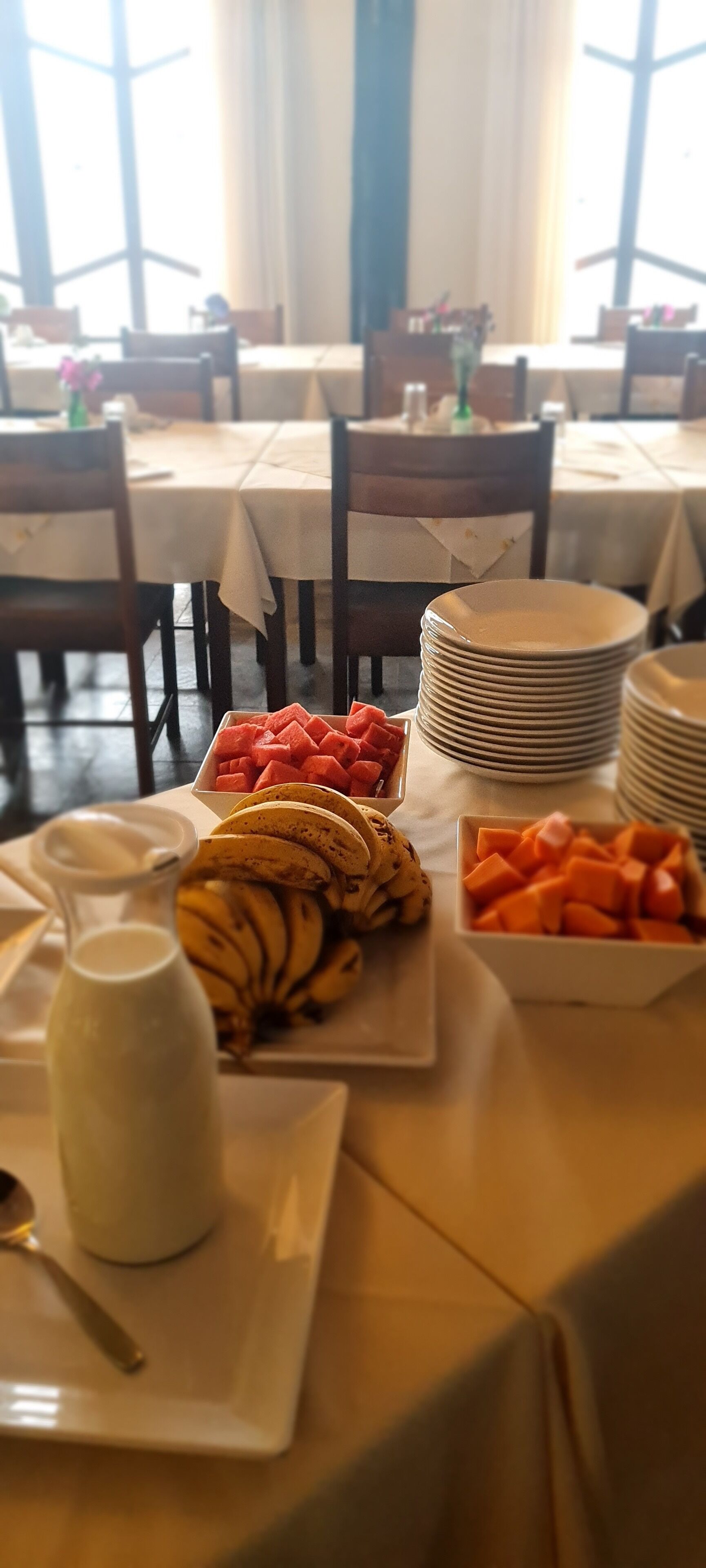 A buffet table with various food items including watermelon, bananas, and a pitcher of milk.